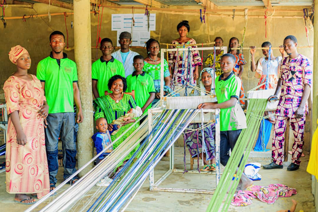 Atelier partenaire de Parakou : jeunes tisserands et tisserandes autour d'un métier à tisser traditionnel, fils de chaîne tendus.